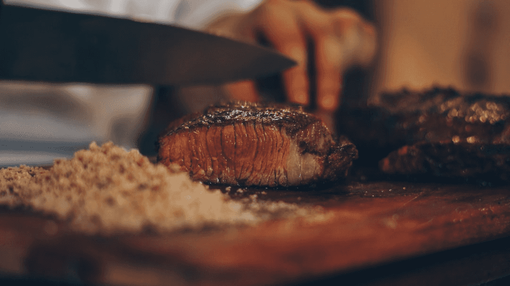 A meat lover uses a blade meat tenderizer to slice a steak on a cutting board.