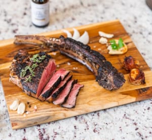 A steak sitting atop a wooden cutting board, ready to be tenderized with a Blade Meat Tenderizer.